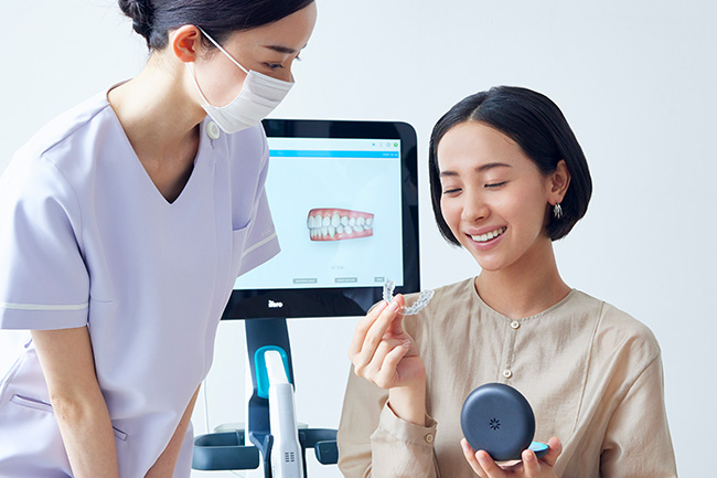歯科矯正のマウスピースを手に持ち説明を受ける女性
